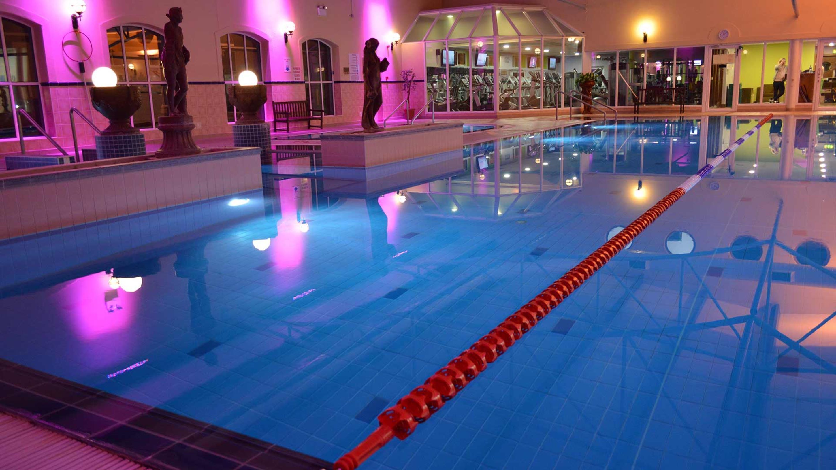 An indoor swimming pool with clear water, a red lane divider, and statues on the walls.