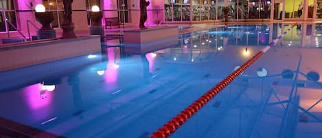 Piscina interior com água cristalina, divisória de pista vermelha e estátuas nas paredes.