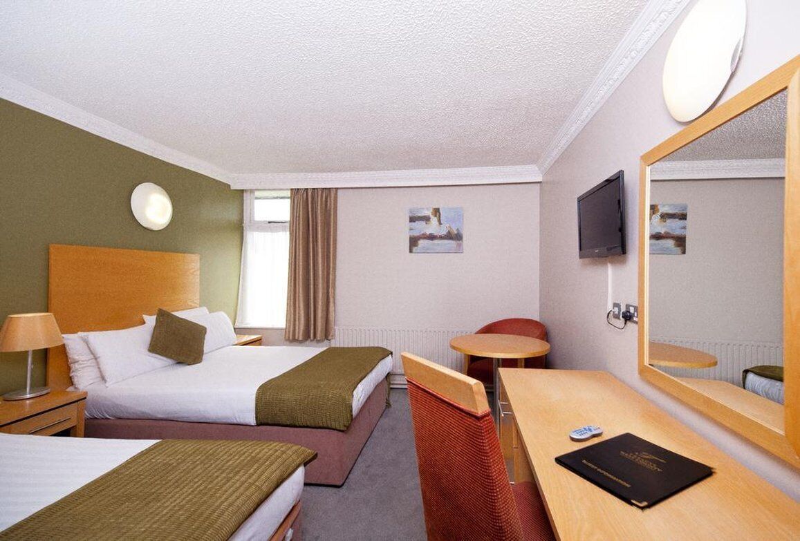 A hotel room with two beds, a desk, a chair, a TV, and a large mirror.