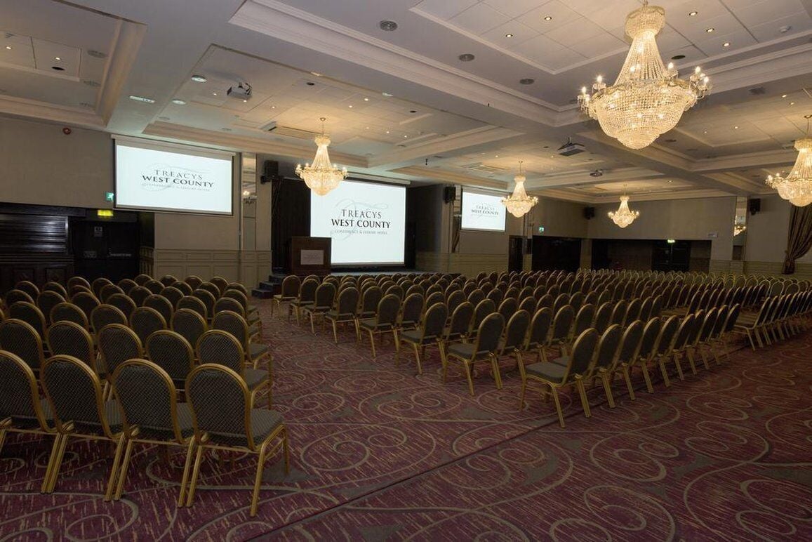 A conference room with rows of chairs, a carpeted floor, and chandeliers.