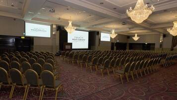 A conference room with rows of chairs, a carpeted floor, and chandeliers.