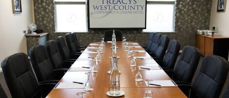 A conference room at Treacy's West County Conference & Leisure Hotel with a long table, black chairs, and a projector screen.