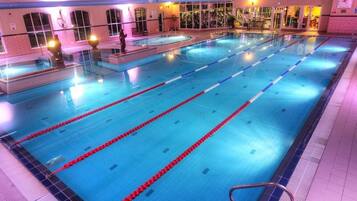 Una gran piscina interior con varias pistas, rodeada de suelo y paredes con azulejos, y equipada con barandillas de seguridad.