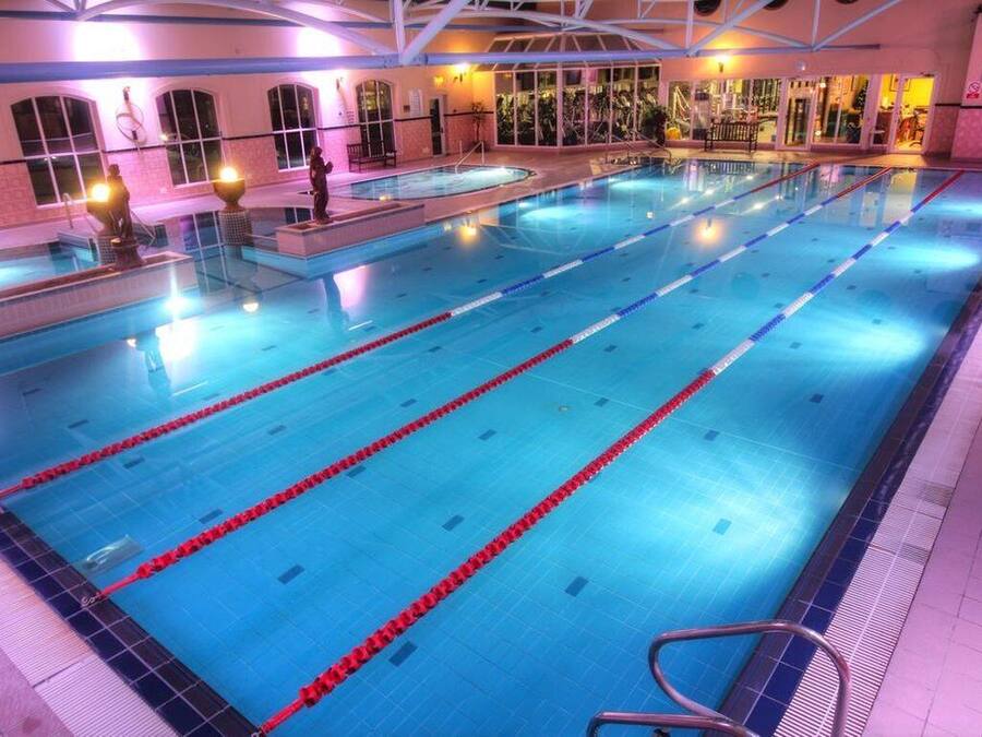 Una gran piscina interior con varias pistas, rodeada de suelo y paredes con azulejos, y equipada con barandillas de seguridad.
