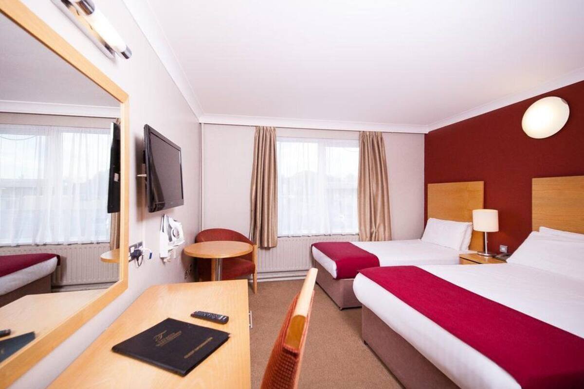 Hotelkamer met een bed, bureau, stoel, televisie en raam met gordijnen.