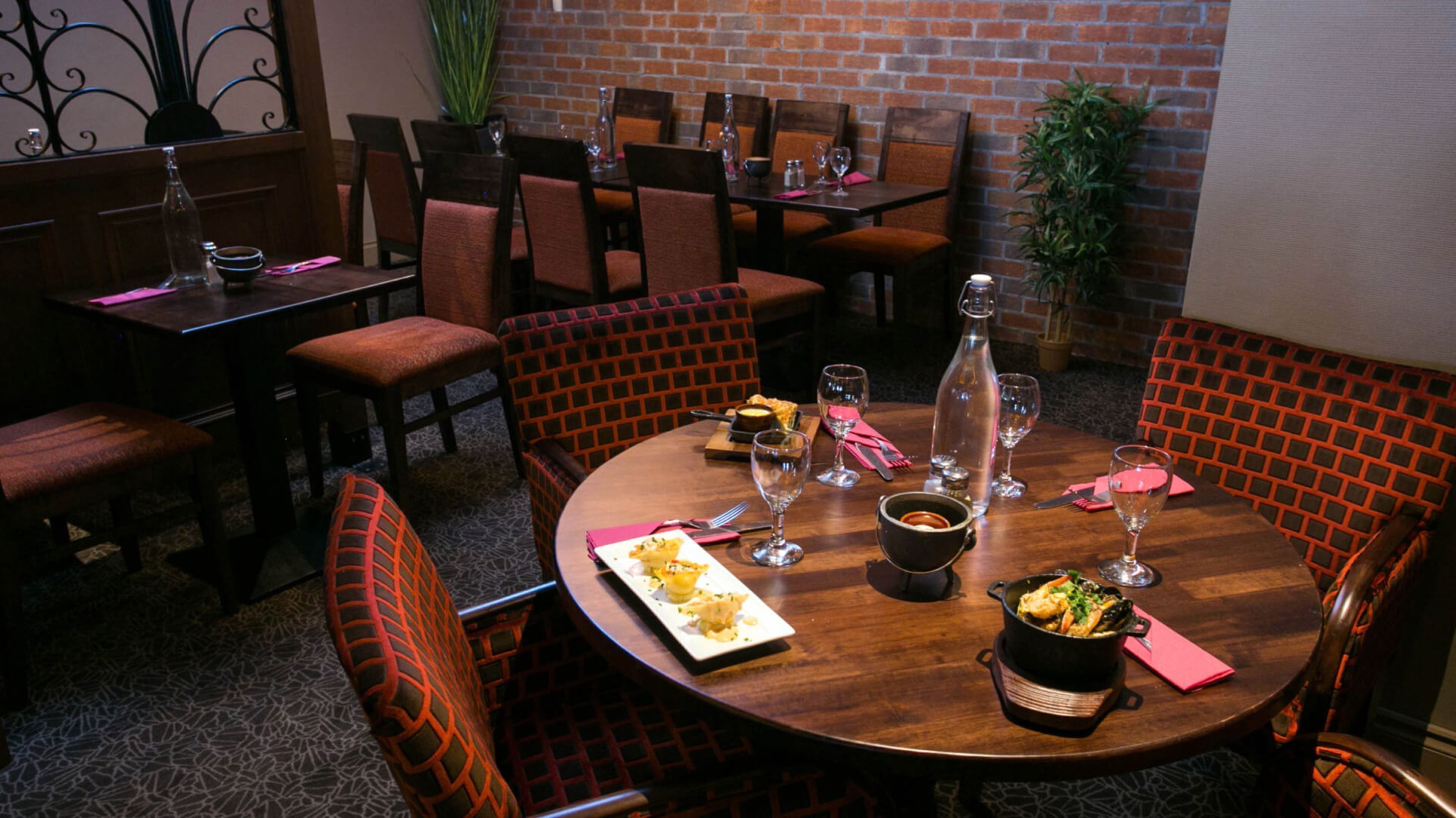 A restaurant with round tables, red cushioned chairs, and a brick wall.