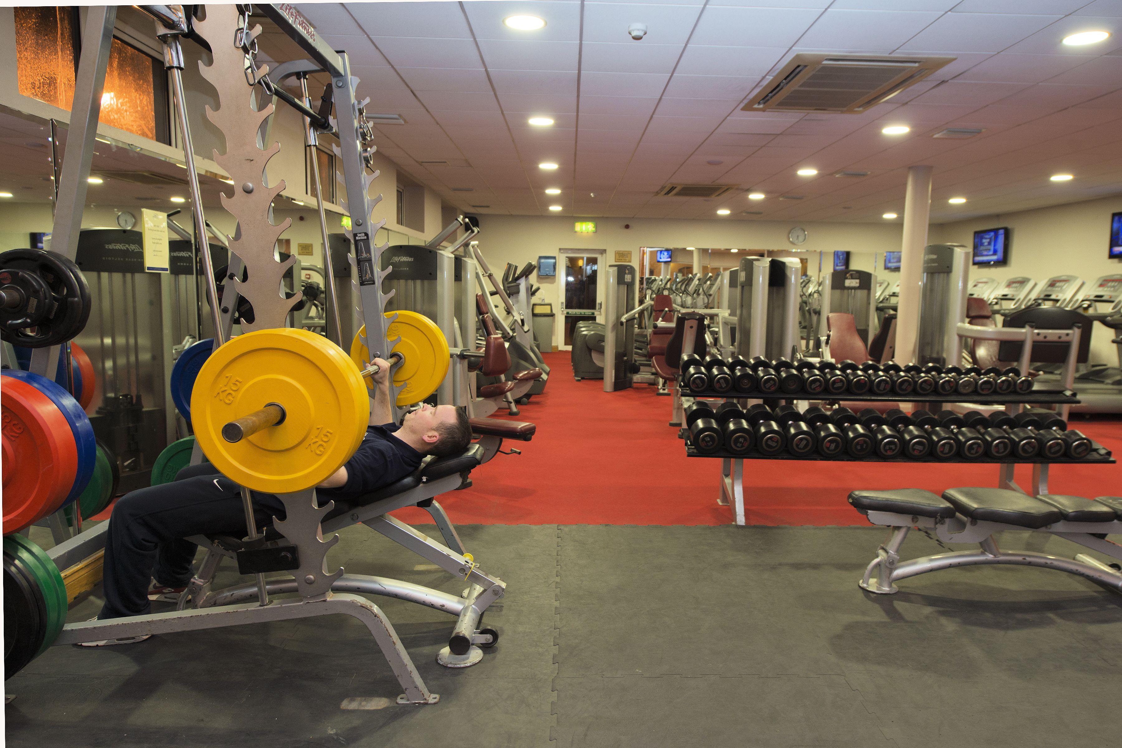 A gym with weightlifting equipment, benches, and dumbbells.