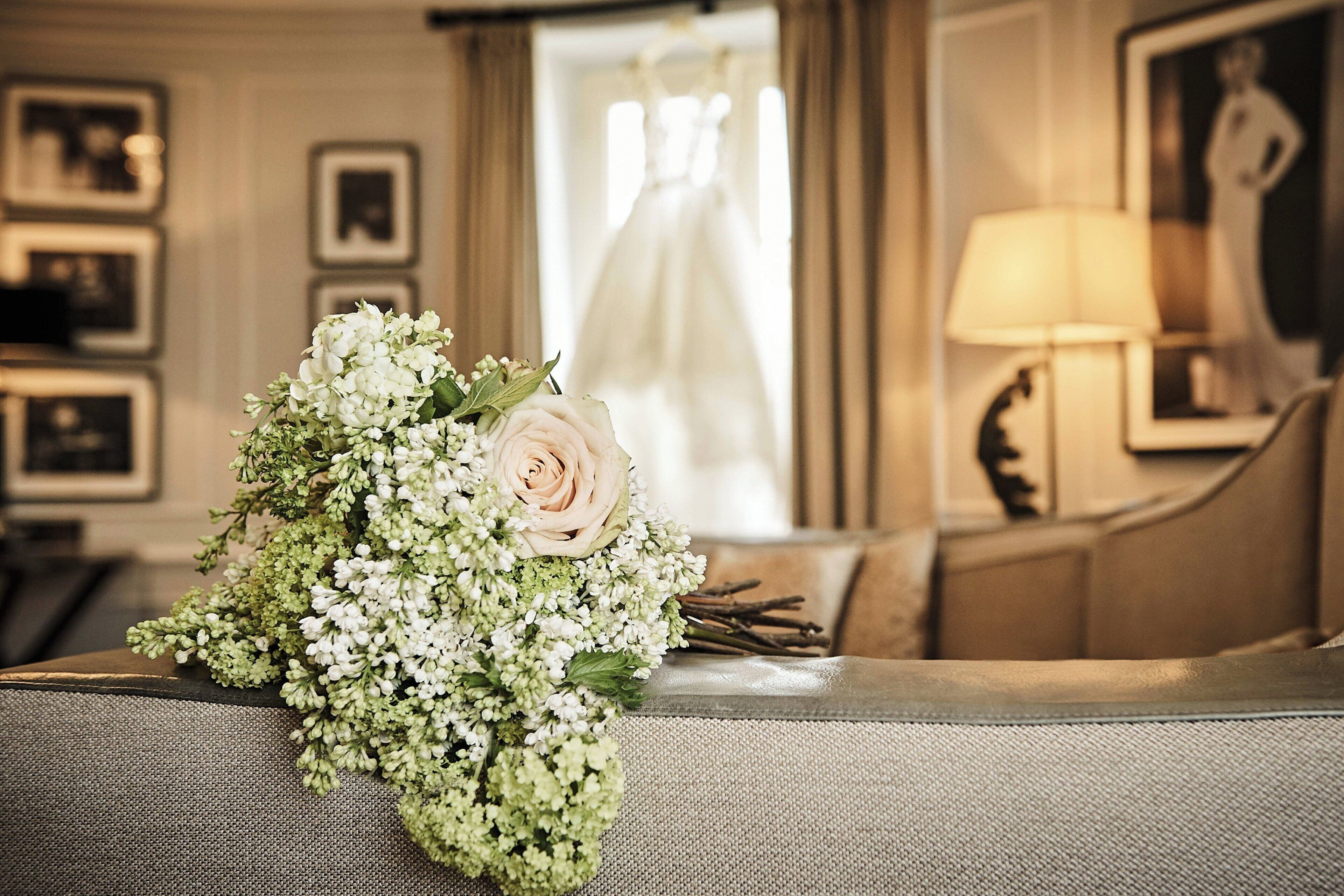 A bouquet of flowers on a grey sofa in a room with a framed picture and a lamp.