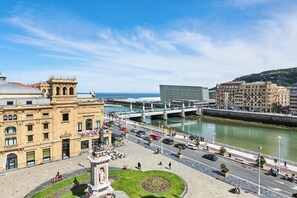 A plaza with a central monument, a river, and a bridge.