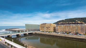 Un paisaje urbano costero con un puente sobre un río, un edificio moderno y un hotel histórico.