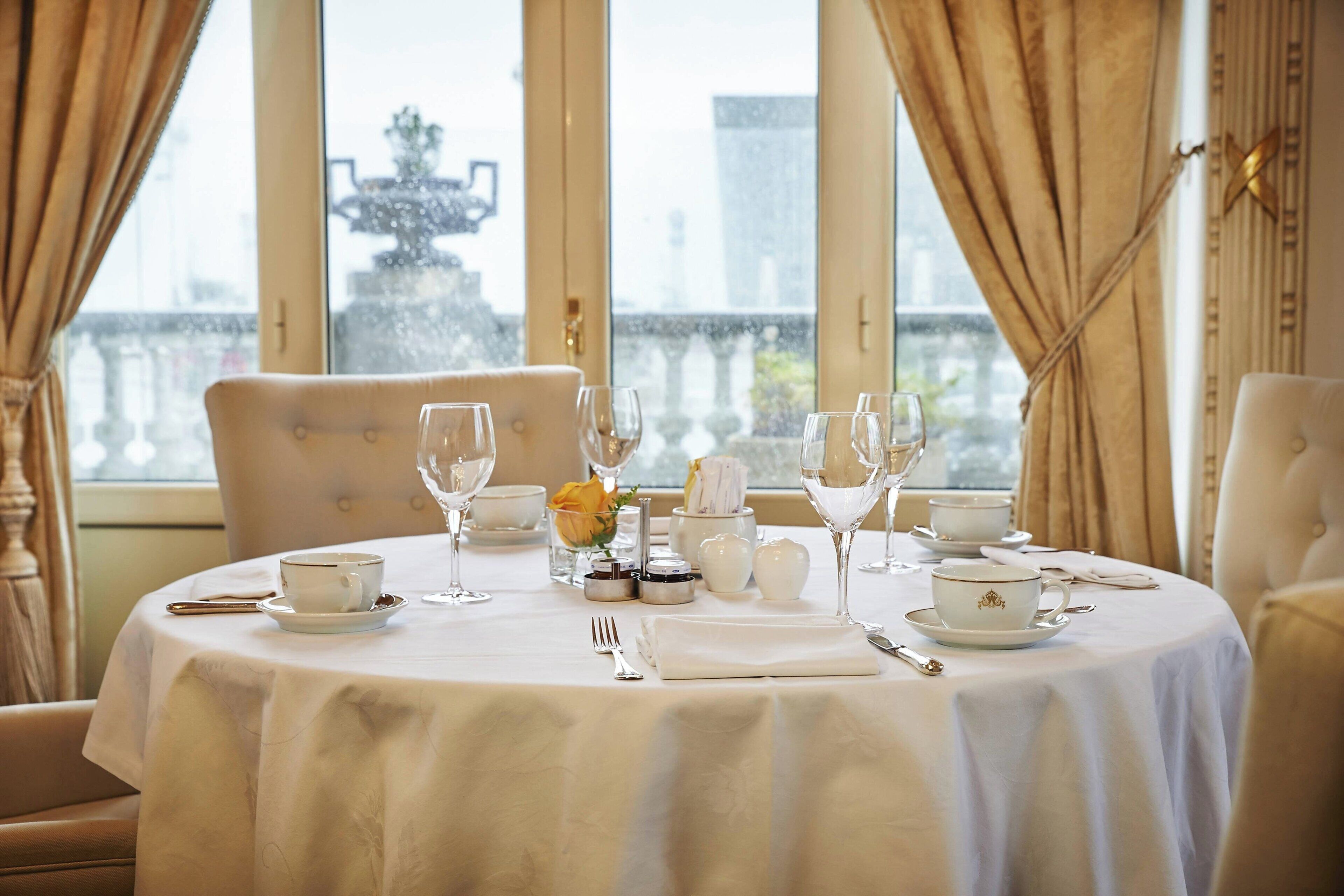 A dining table set for a meal with white tablecloth, plates, cups, and wine glasses.