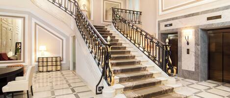 A grand staircase with ornate railings, a marble floor, and a fireplace.