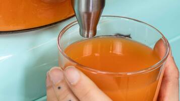 A hand holding a glass with a liquid, possibly tea, being poured from a metallic container.