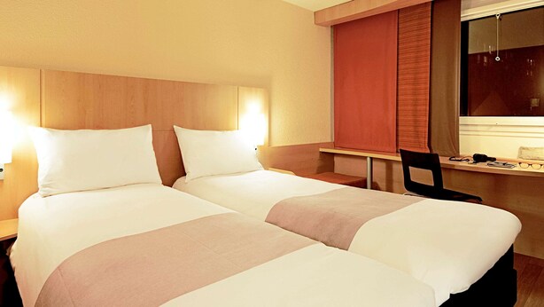 Een hotelkamer met twee bedden, een bureau en een stoel.