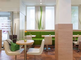 Un interno ristorante moderno con sedute verdi, sedie bianche e tavoli rotondi.