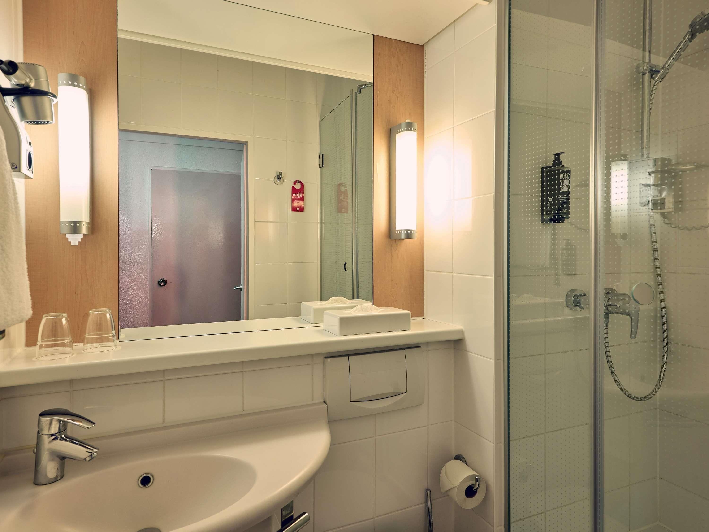 Un baño moderno con un espejo grande, dos lavamanos, ducha y un perchero para toallas.