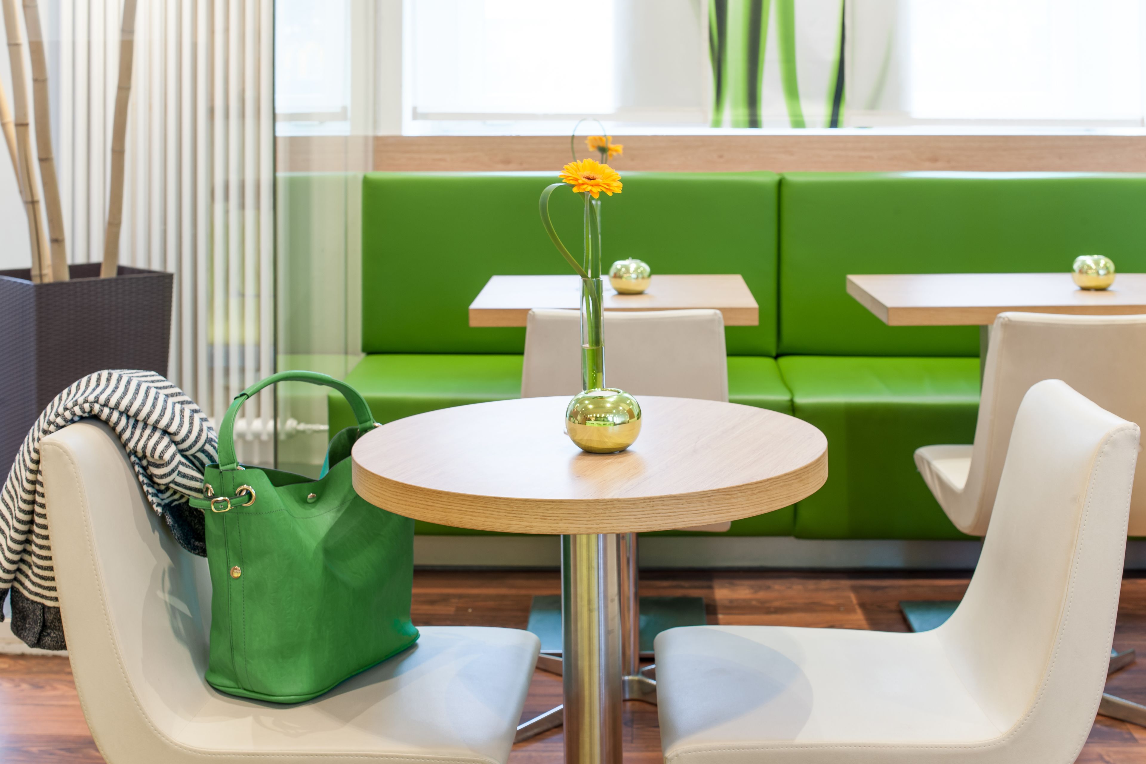 A green sofa, white chairs, and a round table with a vase of flowers.