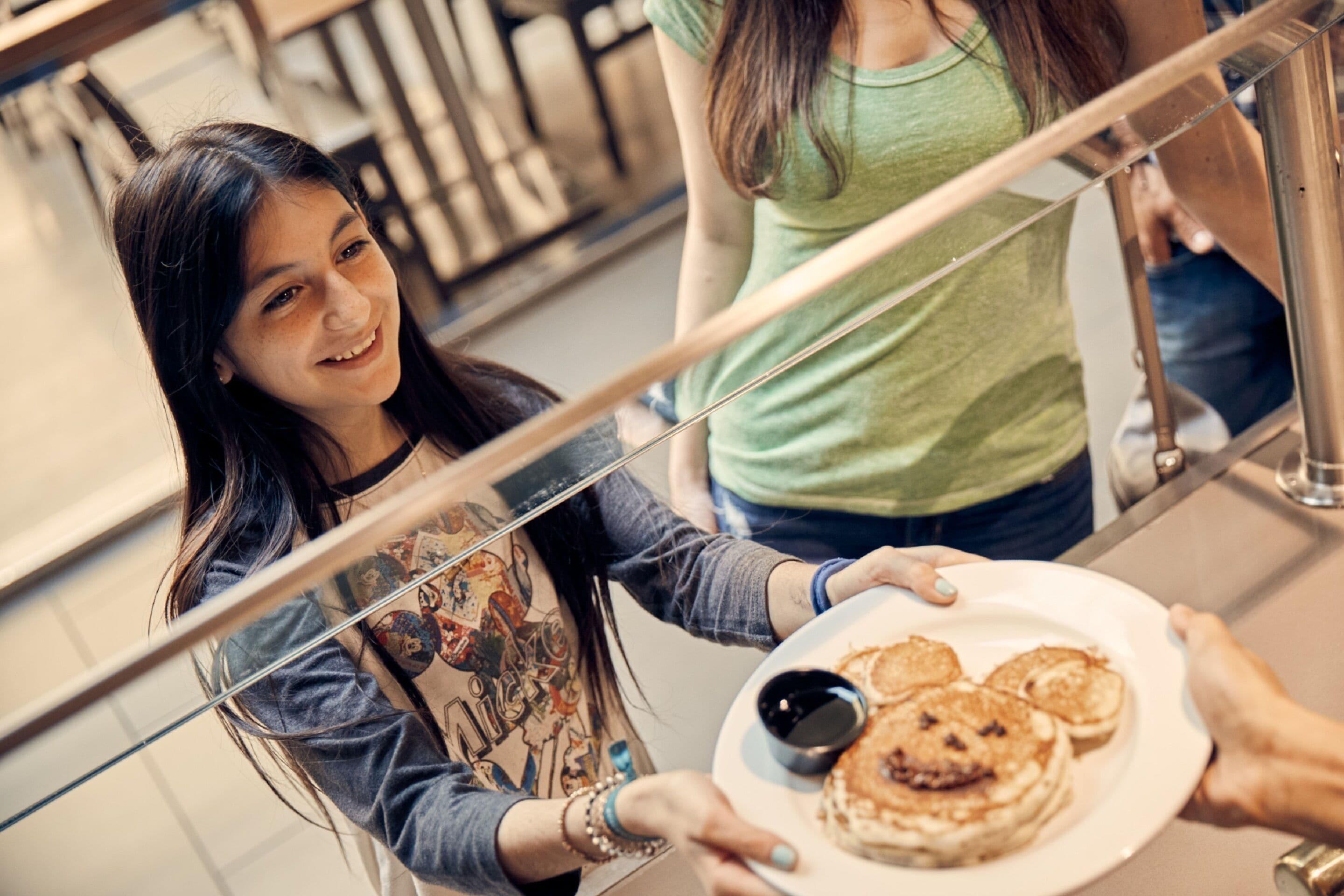A person holding a plate with pancakes and syrup, standing near a railing in a public indoor space.