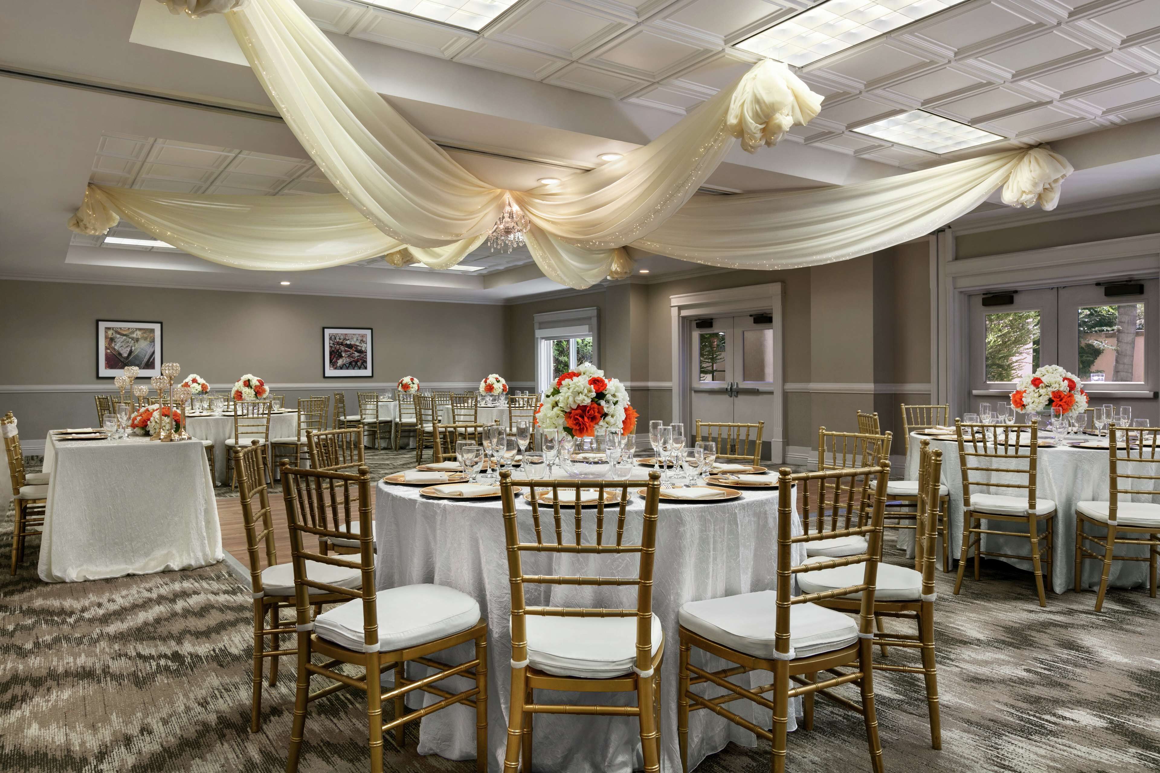 A banquet hall with round tables, gold chairs, and white tablecloths.