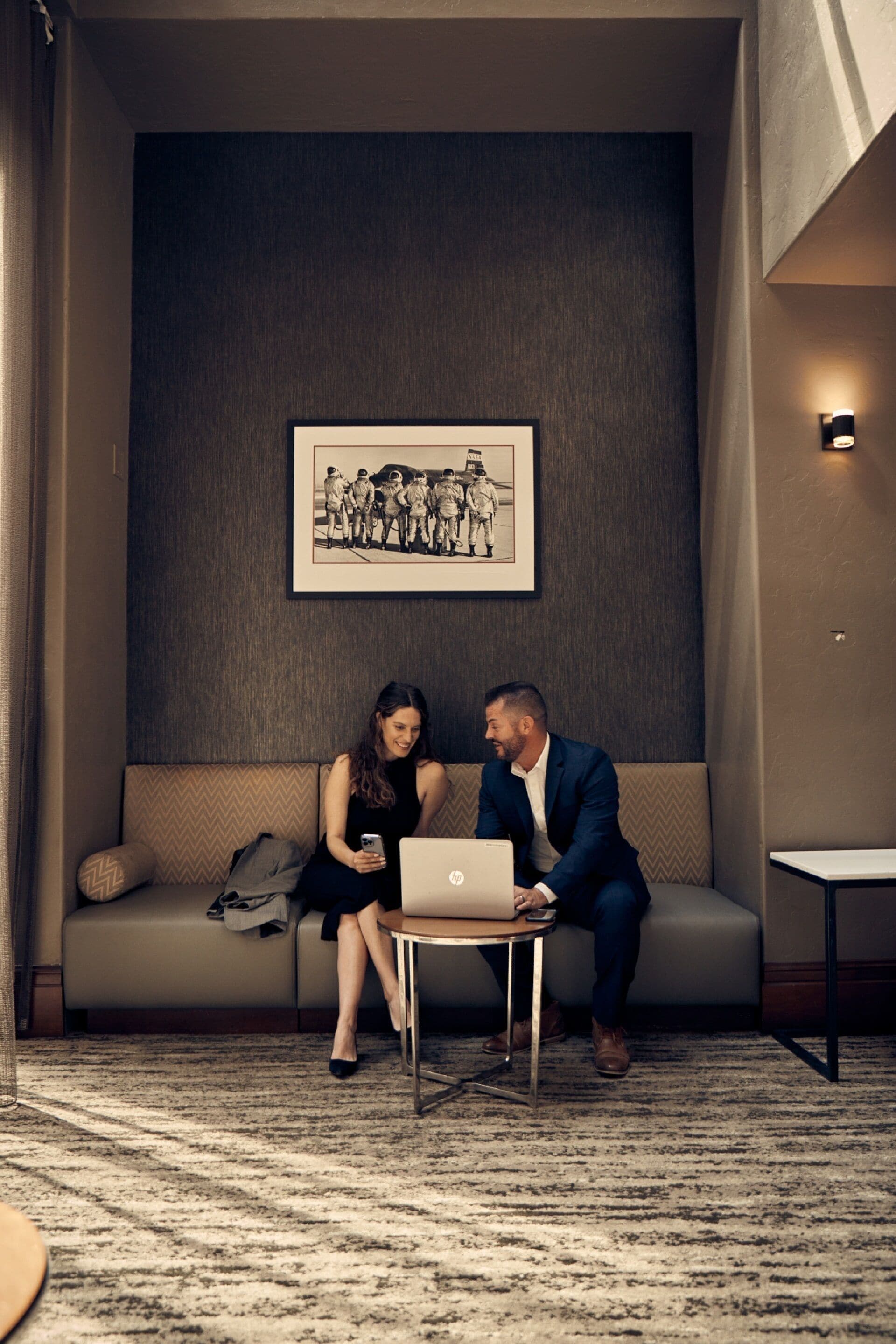 A room with a sofa, a small table, and a laptop. There is a framed picture on the wall.