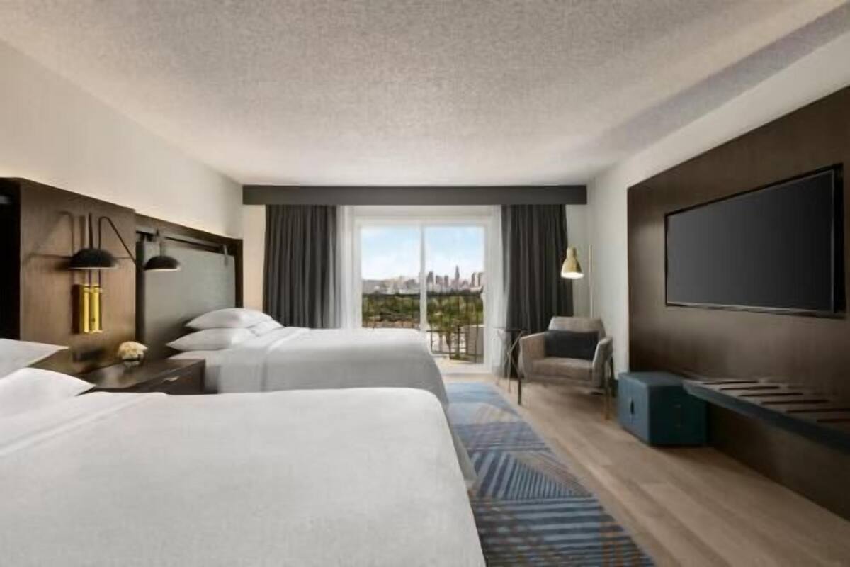 A hotel room with two beds, a large window, a flat-screen TV, and a city view.