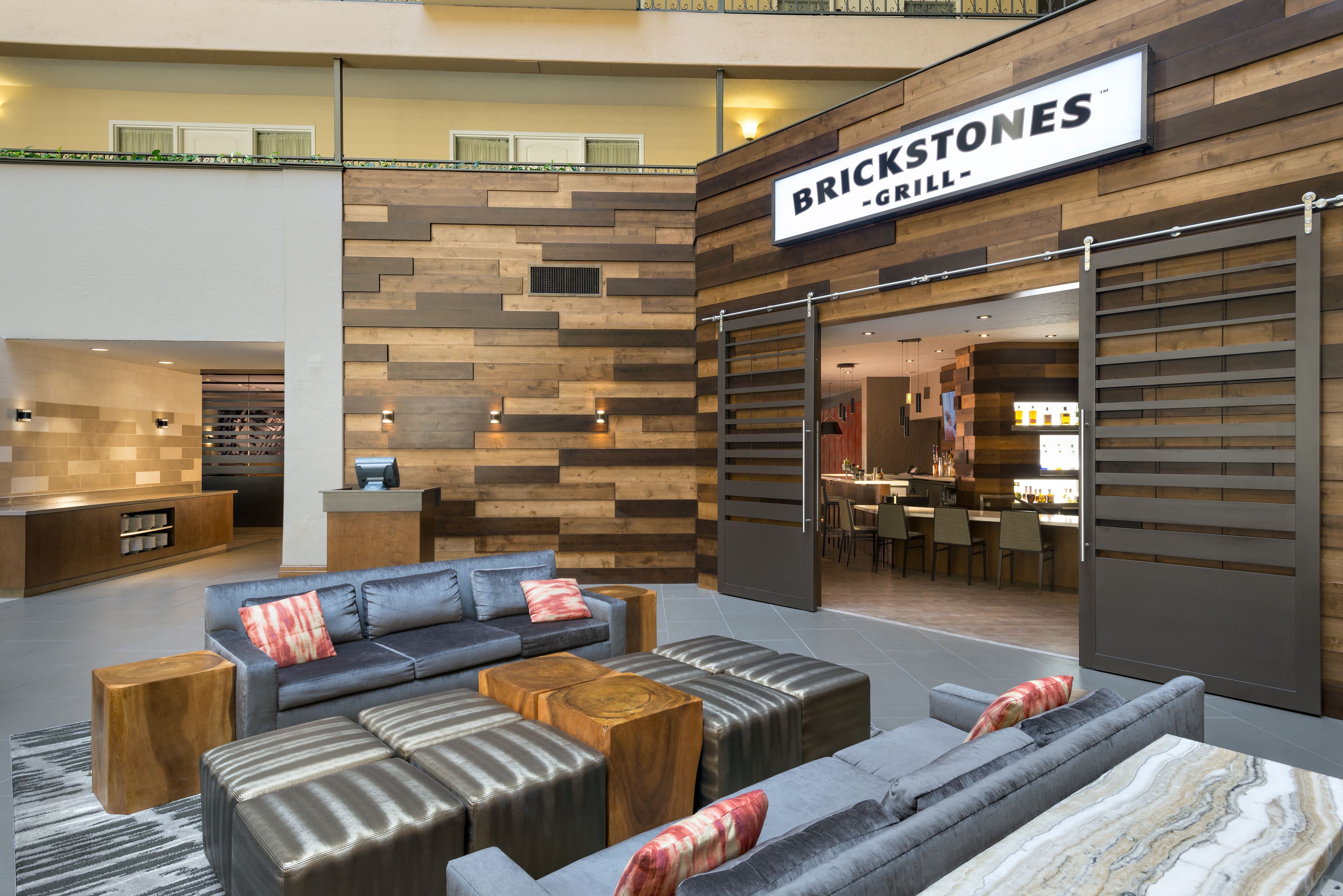 A modern lobby with a seating area, a restaurant named Brickstones Grill, and a bar area.