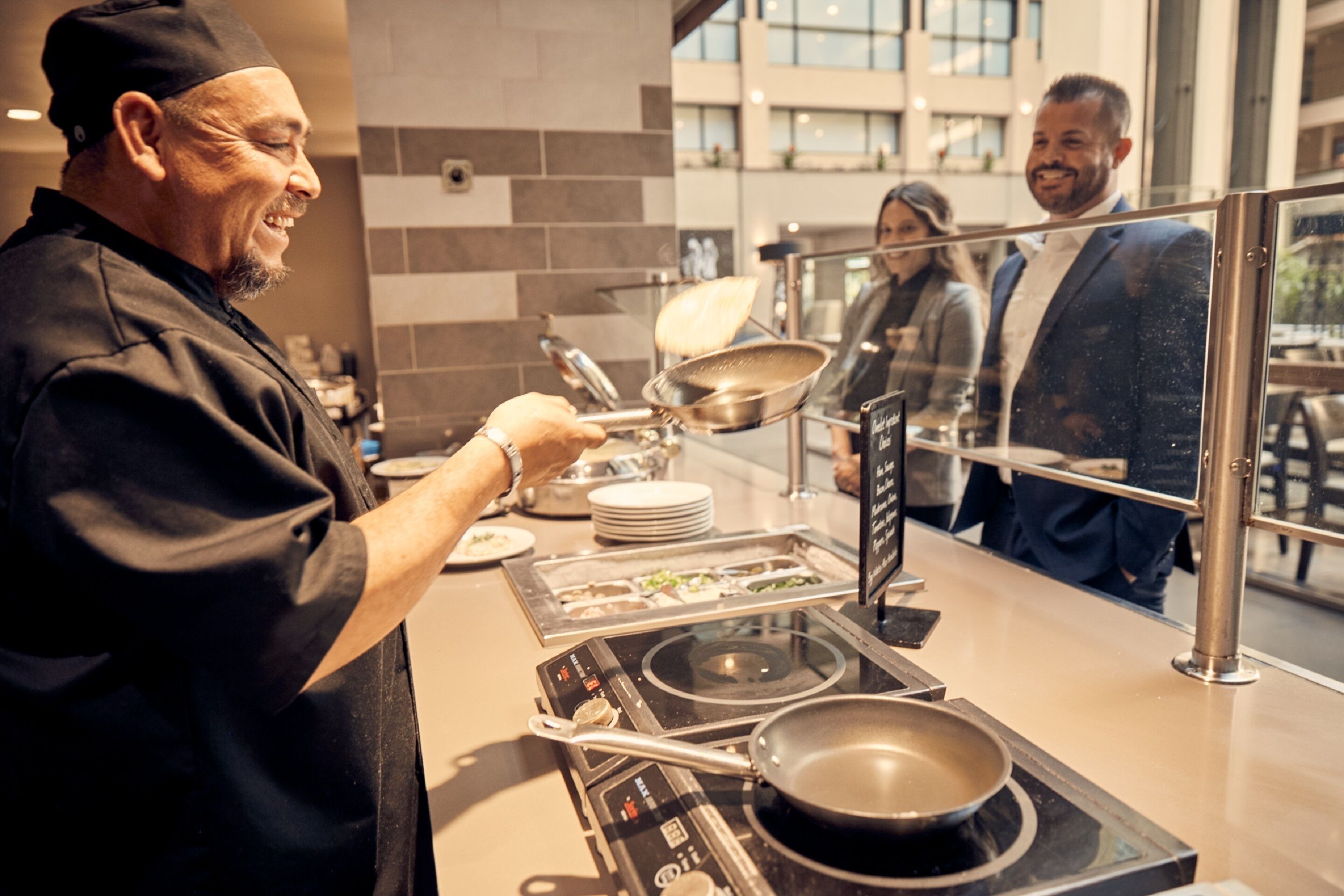 Un buffet avec un chef qui sert les plats, un plan de travail de cuisson en acier inoxydable et une cloison en verre.