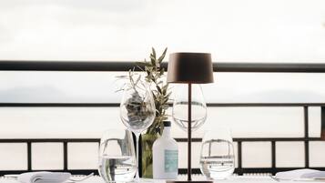 A table set with a water bottle, glasses, and a vase with greenery, overlooking a body of water.