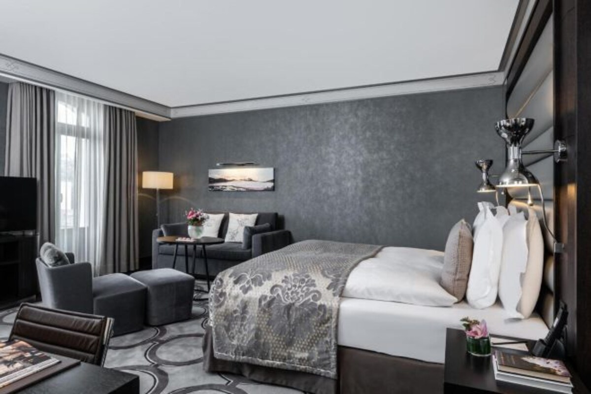 Una habitación de hotel con cama, escritorio, silla, televisión y ventana con cortinas.