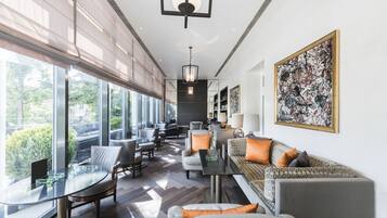 A modern hotel lobby with a long reception desk, seating area, and large windows offering a view of the outdoors.