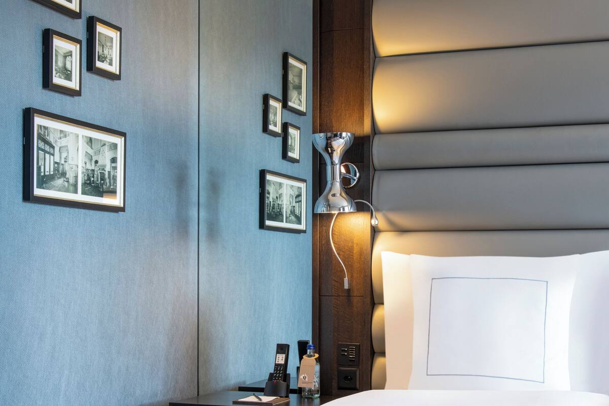 Habitación de hotel con una cama grande, una mesita de noche, una lámpara y cuadros en la pared.