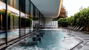 A modern indoor swimming pool with glass walls, lounge chairs, and a waterfall feature. - Royal Savoy Hotel & Spa (Lausanne)