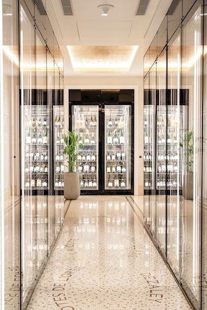Eine moderne Hotellobby mit poliertem Marmorboden, Weinkühlschränken mit Glastüren und einer großen Pflanze in der Mitte.