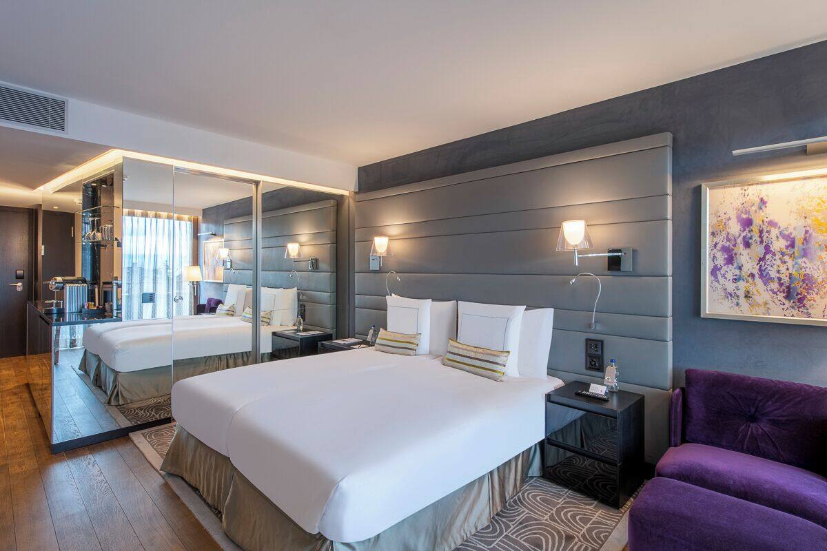 Una habitación de hotel moderna con una cama grande, zona de estar y un espejo.