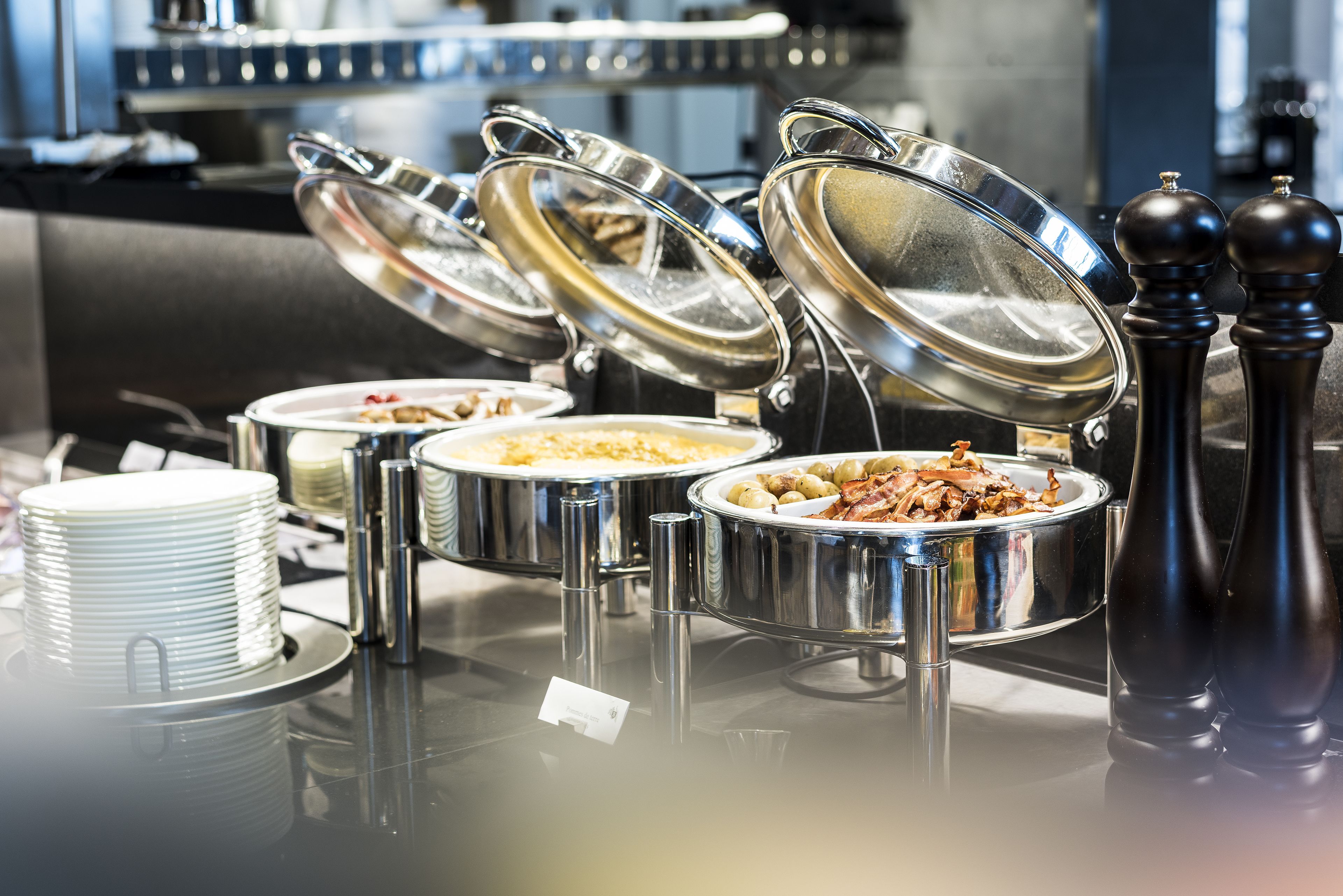 Buffet-style food service with multiple stainless steel serving dishes and lids, arranged on a reflective surface.