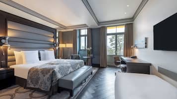 A hotel room with a large bed, a desk, a chair, a small table, and a TV.