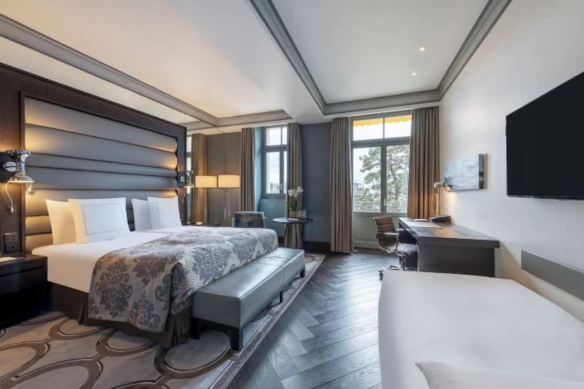 A hotel room with a large bed, a desk, a chair, a bench, and a TV.