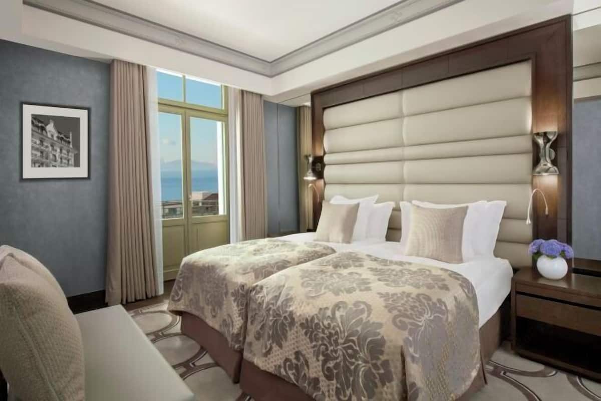 A hotel room with a large bed, a desk, a chair, a window with curtains, and a framed picture on the wall.