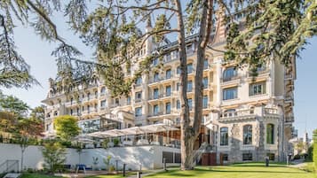 Un hotel grande de varios pisos con estilo arquitectónico clásico, con balcones y un césped cuidado.