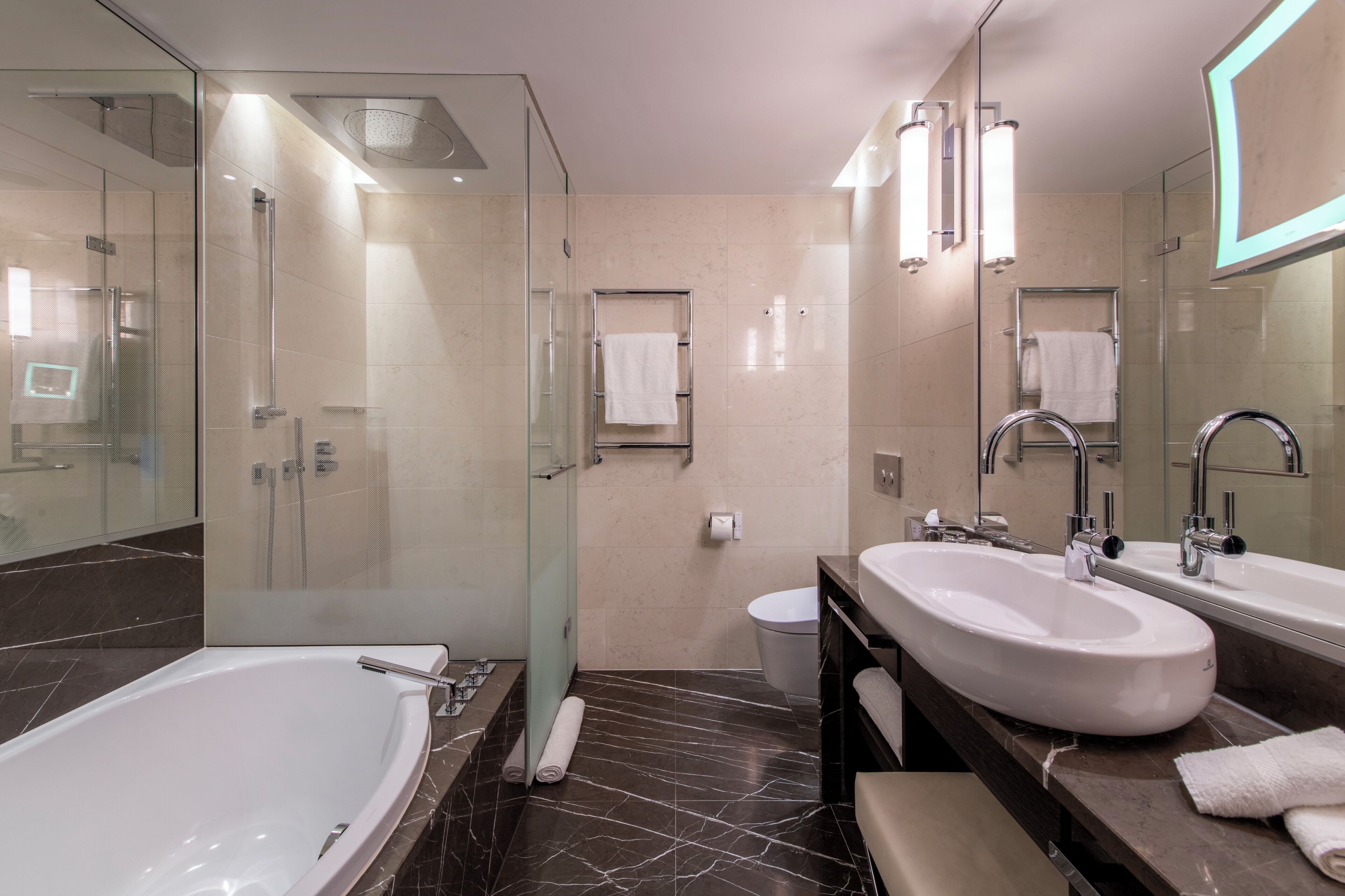 A modern bathroom with a glass-enclosed shower, a large bathtub, and two sinks.