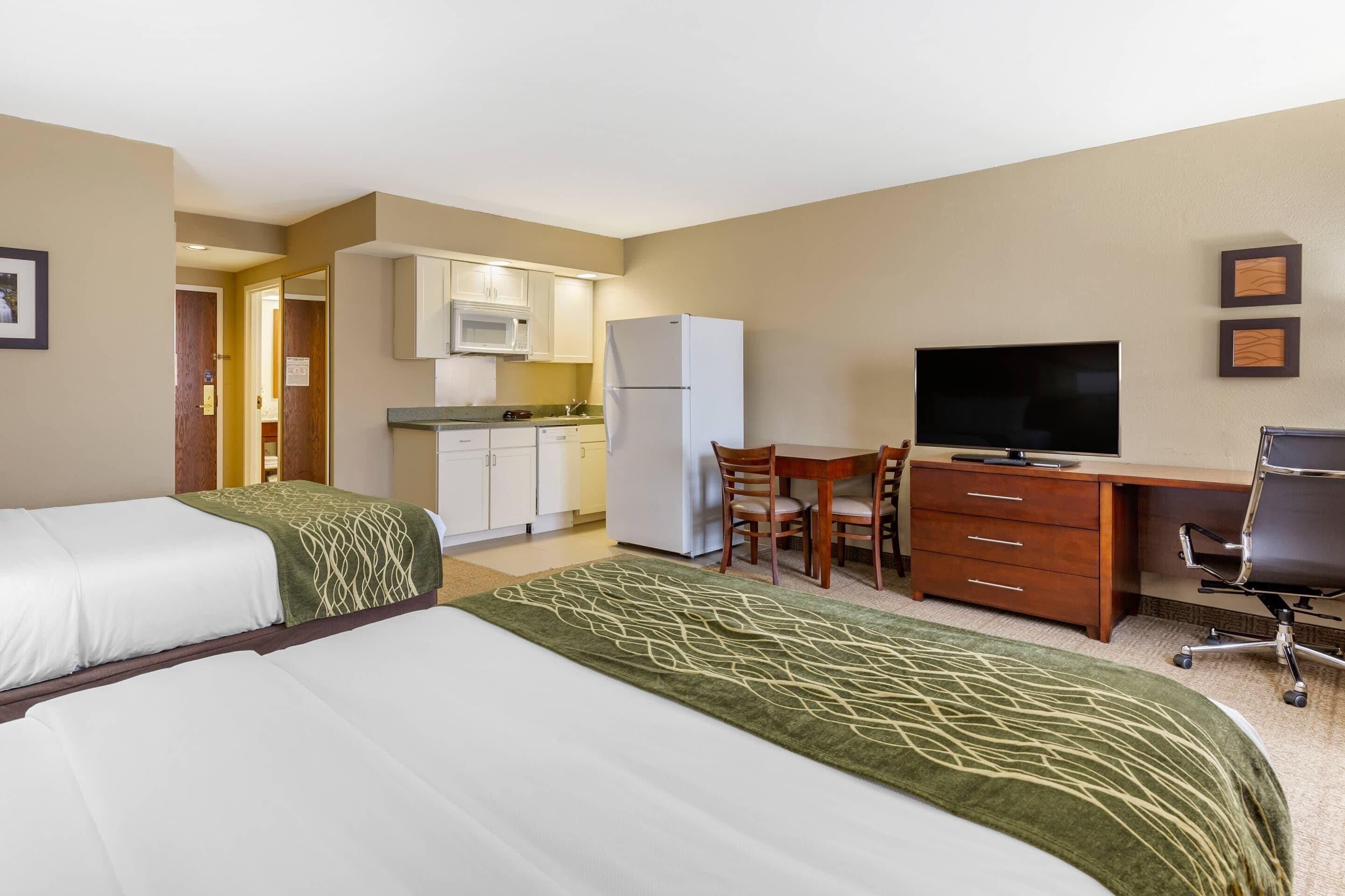 Una habitación de hotel con dos camas, un escritorio, un televisor y un kitchenette.