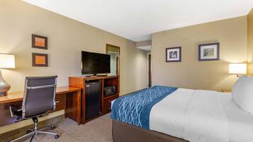 Una habitación de hotel con cama, escritorio, silla, televisor y microondas.