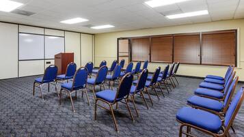 Un salón de conferencias con filas de sillas azules, una pizarra y un atril de madera.