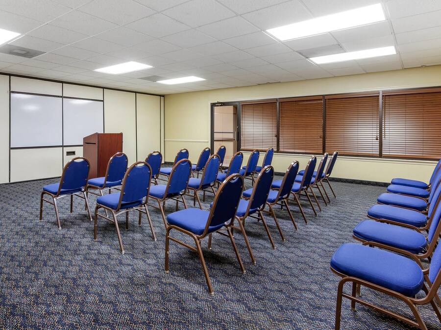 Un salón de conferencias con filas de sillas azules, una pizarra y un atril de madera.