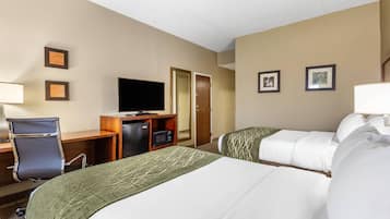 Una habitación de hotel con dos camas, un escritorio con una computadora, un televisor y una puerta.