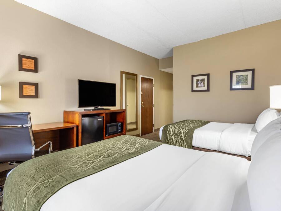 Une chambre d’hôtel avec deux lits, un bureau avec un ordinateur, une télévision et une porte.