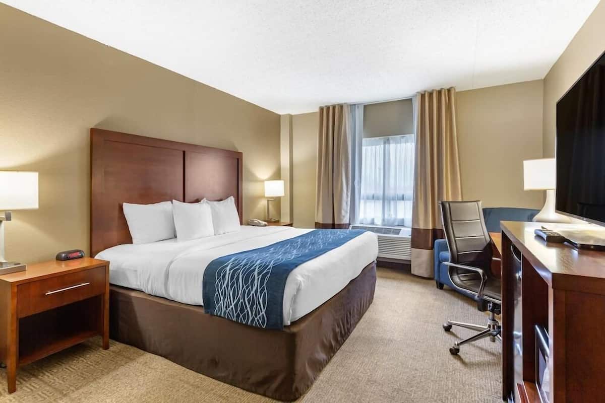 A hotel room with a large bed, bedside tables, a desk, a chair, and a television.