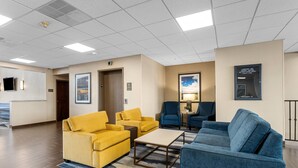 A hotel lobby with a reception desk, yellow and blue sofas, a coffee table, and framed artwork on the walls. - Comfort Inn Aikens Center (Martinsburg)