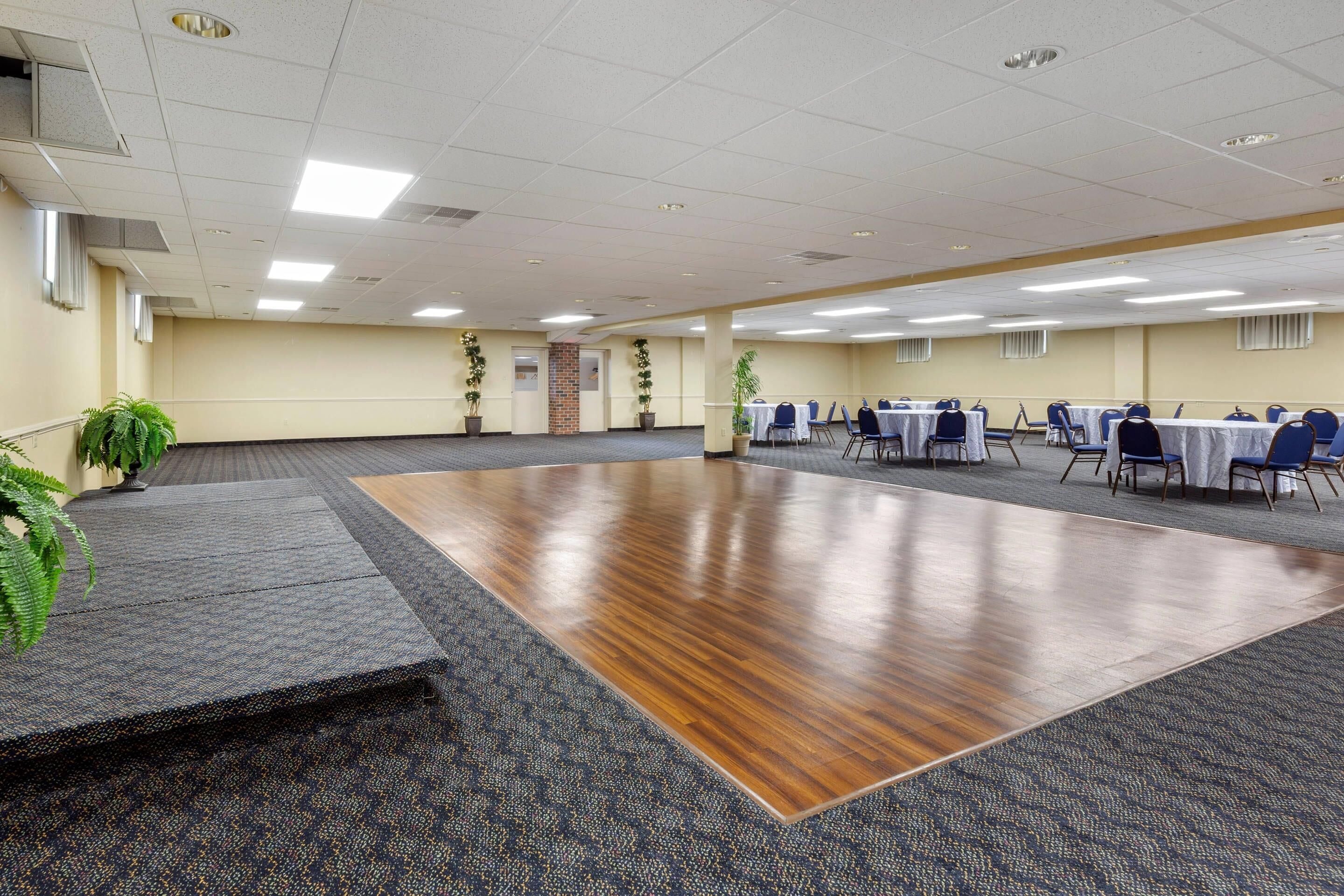 Une grande salle de conférence dotée d’un plancher en bois, de zones recouvertes de moquette et de tables avec des chaises.