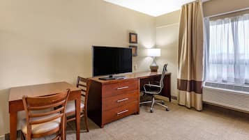 Habitación de hotel con escritorio de madera, una silla, televisor, lámpara y ventana con cortinas.